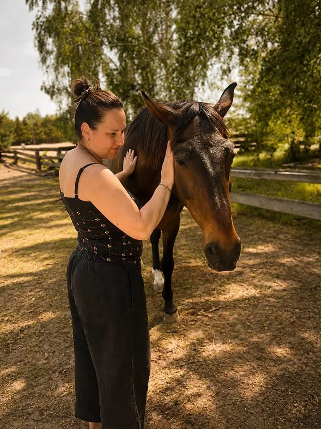 Žena v ohradě jemně hladí hnědého koně po hlavě a hřívě